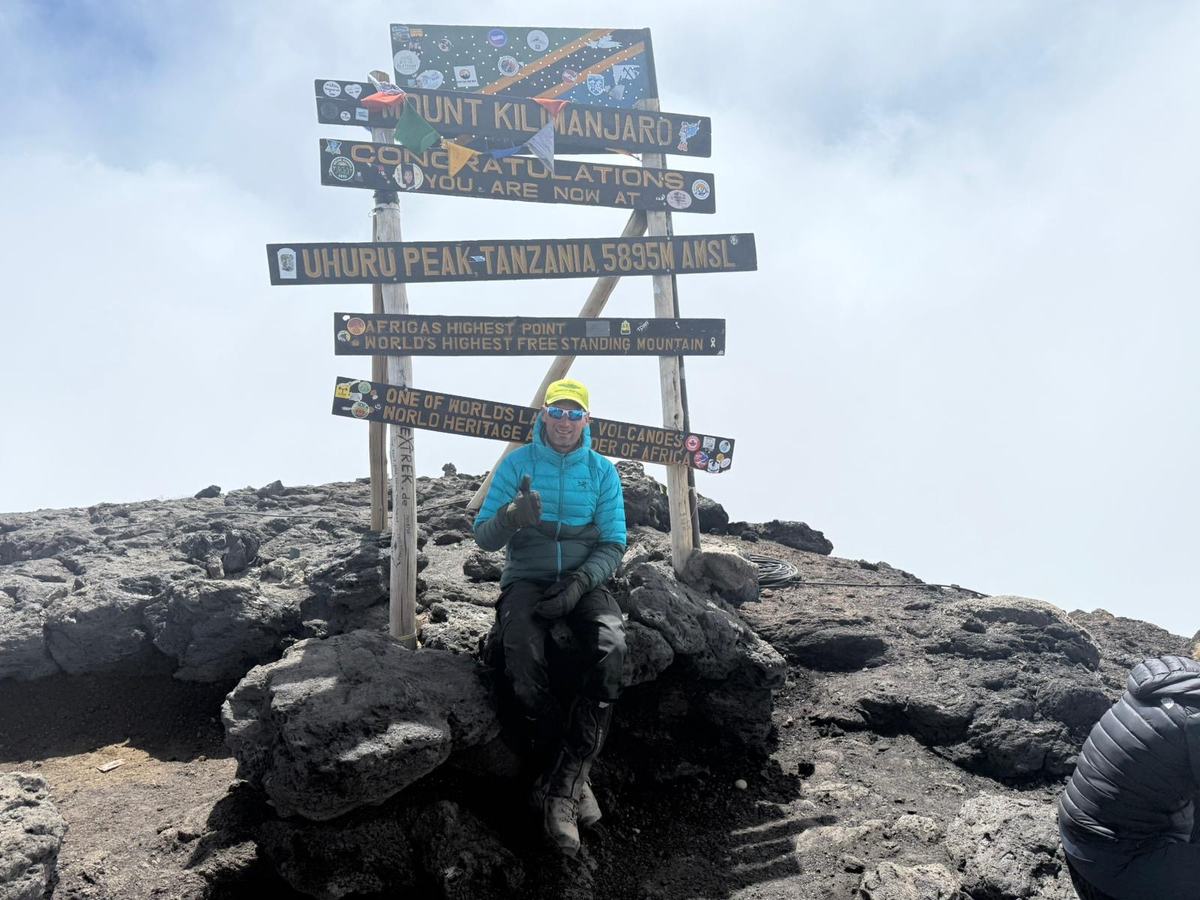 Koen in een turquoise jas bij het bord op Uhuru Peak, de top van de Kilimanjaro