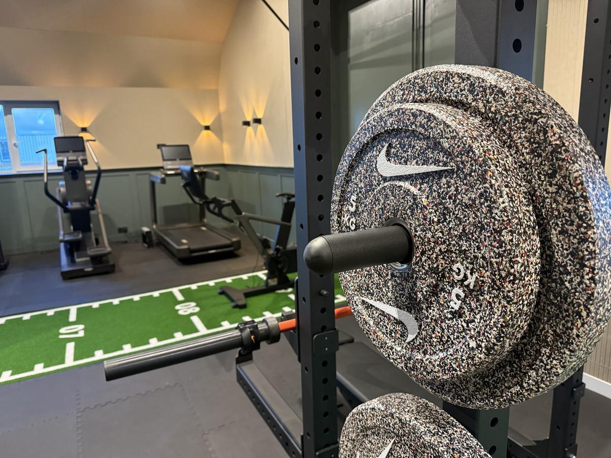 Halterschijf van 5 kilo in het rek, met de sprintbaan en cardioapparaten erachter